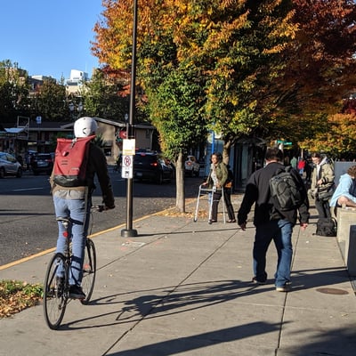 Bicyclists and pedestrians, including one person using a walker or mobility device, navigate the PSU campus.